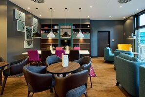 A modern lounge area with seating, a bookshelf, and a menu stand.