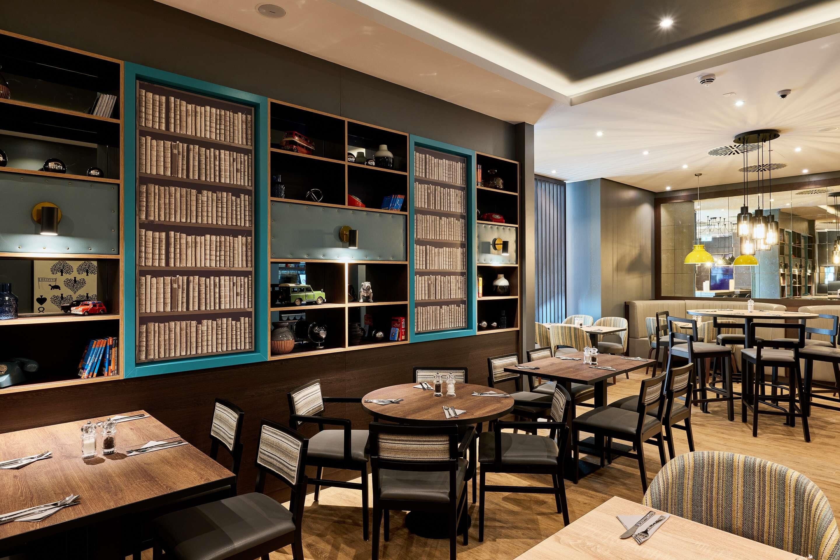 Una biblioteca con estanterías, un comedor con mesas y sillas, y una zona de bar con asientos.