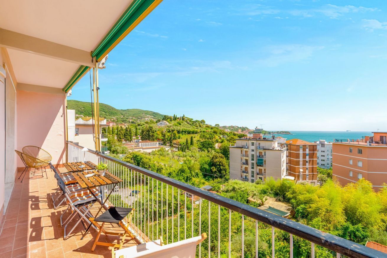 A balcony with outdoor furniture, a view of a coastal town, and buildings in the background.