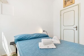Ein Zimmer mit einem Bett, einem blauen Kopfkissen und ordentlich gefalteten weißen Handtüchern.