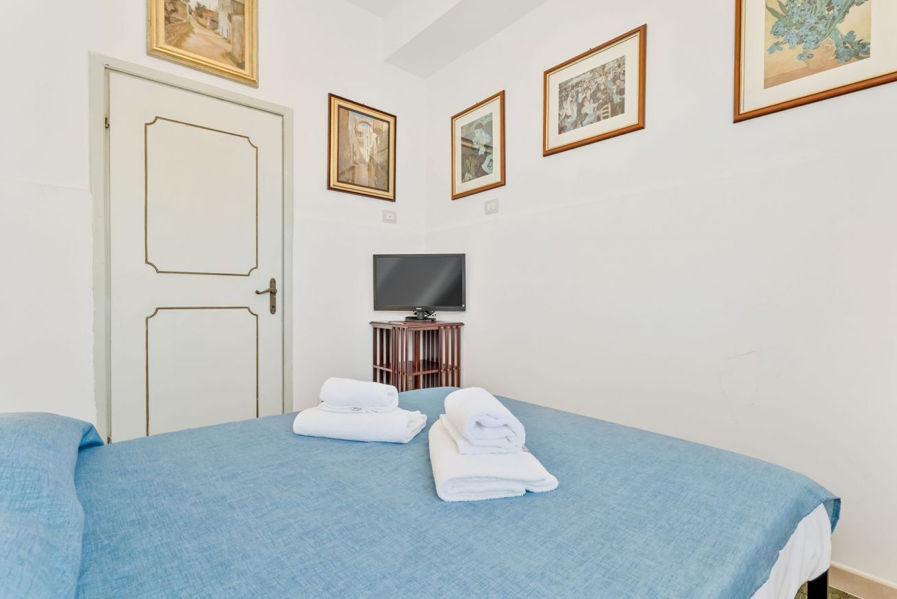 Une chambre d’hôtel avec un lit, deux serviettes, un téléviseur posé sur un meuble et des tableaux encadrés accrochés au mur.