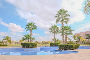 A swimming pool area with palm trees and a clear sky. - Luxury 2BD in Prestigia Jade with Pool and Golf View (Marrakech)