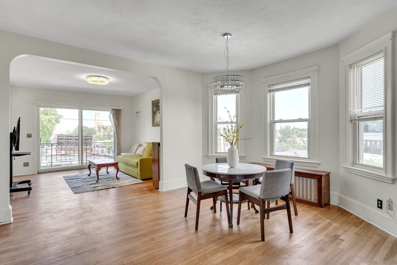 A spacious living room with a round dining table, a green sofa, and a chandelier.
