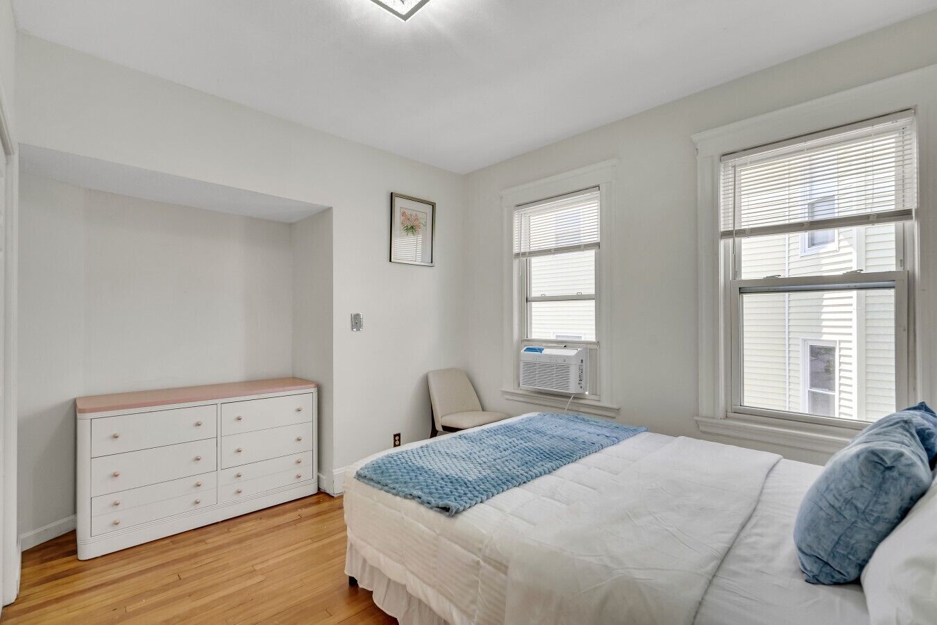 A bedroom with a bed, dresser, chair, and windows.