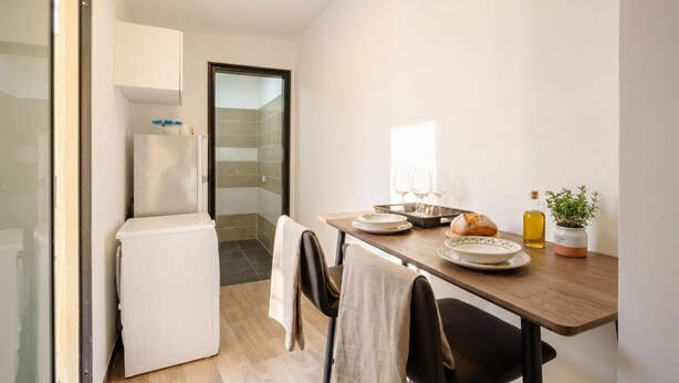 A compact kitchen with a refrigerator, a dining table with chairs, and a small potted plant. - ALL Covi del Viaggiatore – Elegant 2-Bedroom Stay in Bari (Bari)