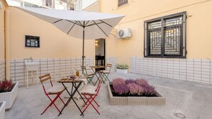 A patio with a table and chairs, a white umbrella, and a planter with purple flowers. - ALL Covi del Viaggiatore – Elegant 2-Bedroom Stay in Bari (Bari)