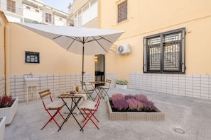 A patio with a table and chairs, a white umbrella, and a planter with purple flowers. - ALL Covi del Viaggiatore – Elegant 2-Bedroom Stay in Bari (Bari)