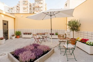 An outdoor patio with a table and chairs, surrounded by potted plants and a large umbrella. - ALL Covi del Viaggiatore – Elegant 2-Bedroom Stay in Bari (Bari)
