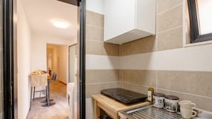 A compact kitchen with a built-in induction cooktop, a small wooden table with a cloth, and a dining area in the background. - ALL Covi del Viaggiatore – Elegant 2-Bedroom Stay in Bari (Bari)