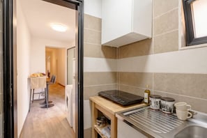 A compact kitchen with a built-in induction cooktop, a small wooden table with a cloth, and a dining area in the background. - ALL Covi del Viaggiatore – Elegant 2-Bedroom Stay in Bari (Bari)
