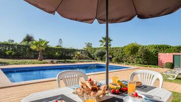 Desayuno junto a la piscina, con una mesa, sillas y una variedad de comida y bebidas.