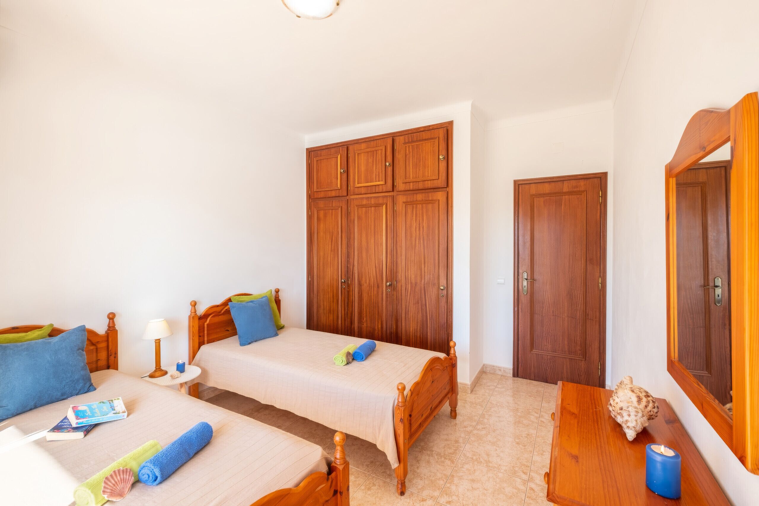 Ein Schlafzimmer mit zwei Betten, einem Holzschrank, einer Holztür und einem kleinen Tisch mit einer Kerze.