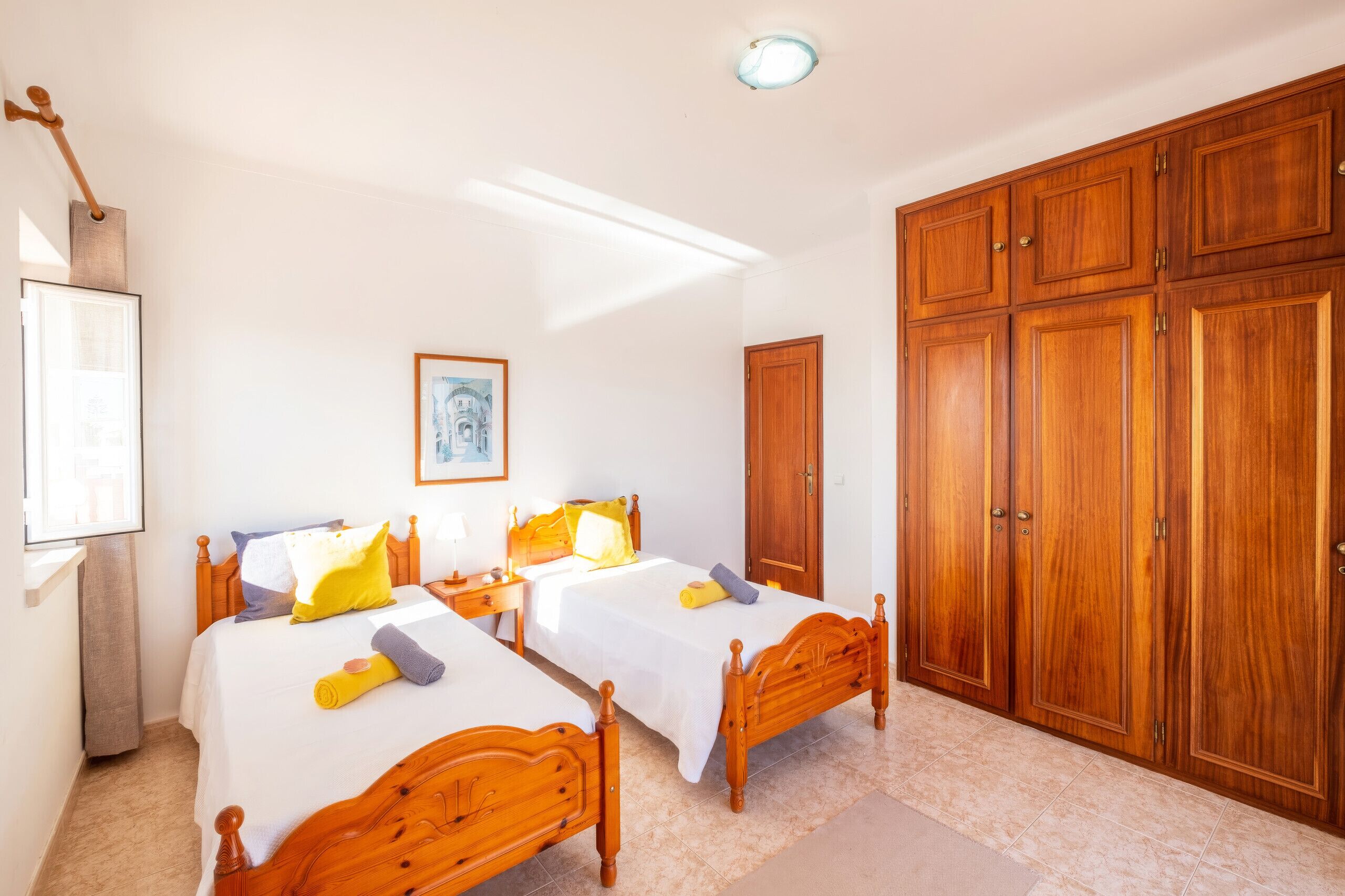 A bedroom with two wooden beds, a wardrobe, and a framed picture on the wall.