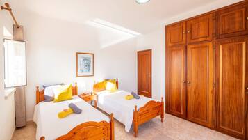 A bedroom with two wooden beds, a wardrobe, and a framed picture on the wall.