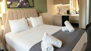 A hotel room with a bed, pillows, a desk, a chair, and a towel on the bed. - Plaka Luminous Deluxe Suite - Located innthe heart of Athens (Athina)