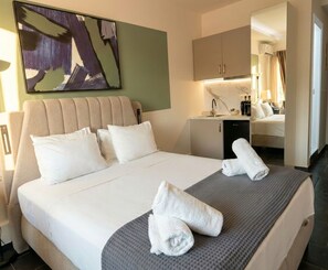 A hotel room with a bed, pillows, a desk, a chair, and a towel on the bed. - Plaka Luminous Deluxe Suite - Located innthe heart of Athens (Athina)