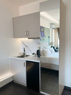 A compact hotel room with a kitchenette, a bed, and a large mirror reflecting the room. - Plaka Luminous Deluxe Suite - Located innthe heart of Athens (Athina)