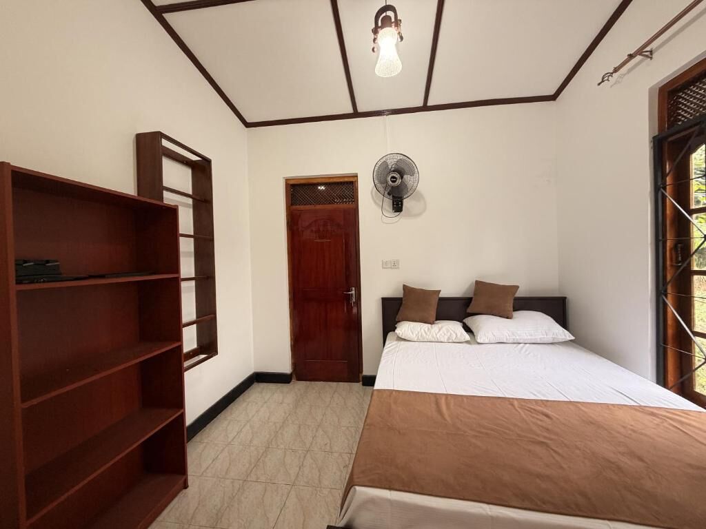 A bedroom with a bed, a wooden shelf unit, a door, and a ceiling fan.