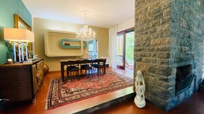 Un espace repas comprenant une table et des chaises, un lustre, un tapis et une cheminée en pierre.