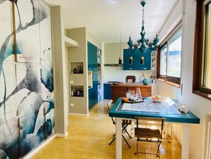 Una cocina moderna con armarios color turquesa, una mesa de comedor con sillas y un cuadro abstracto grande en la pared.
