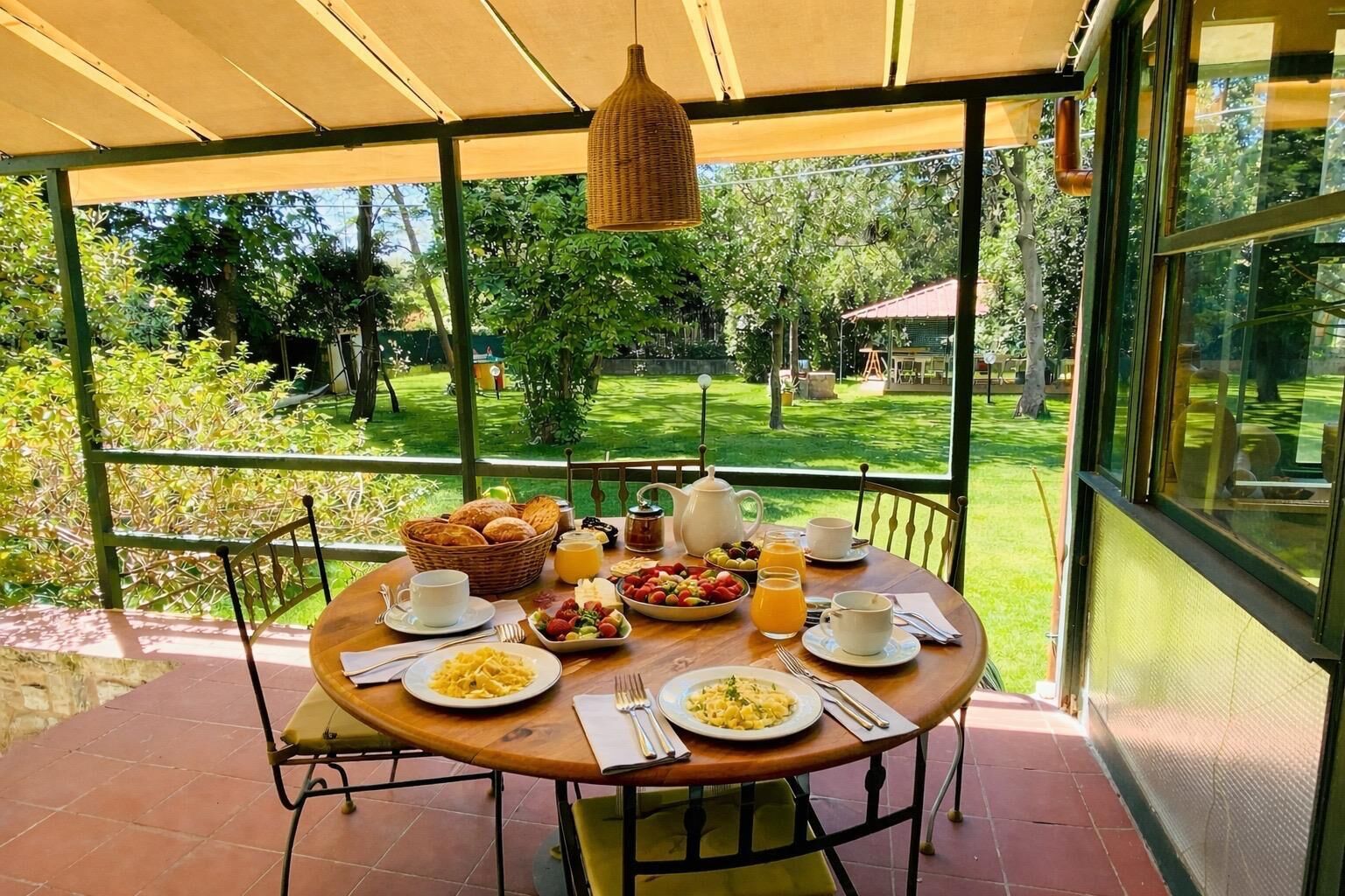 A covered outdoor dining area with a table set for breakfast, including plates of food, drinks, and a basket of bread.