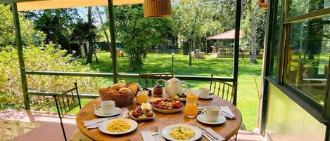A covered outdoor dining area with a table set for breakfast, including plates of food, drinks, and a basket of bread.