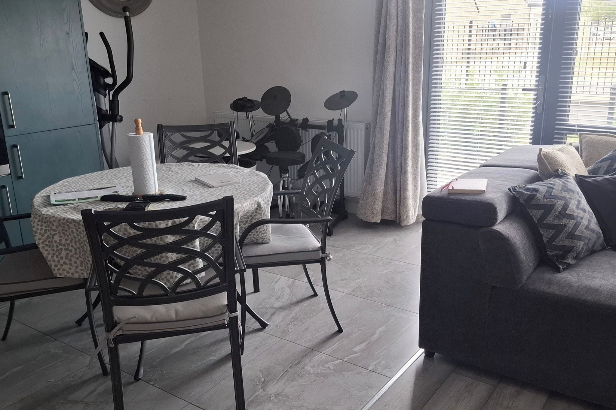 A modern living room with a dining area, featuring a sofa, chairs, a table, and a window with blinds.