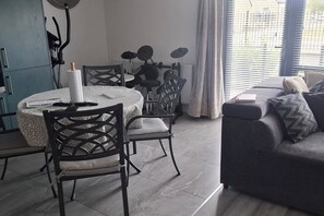 Una sala de estar moderna con comedor, que incluye un sofá, sillas, una mesa y un ventanal con persianas.