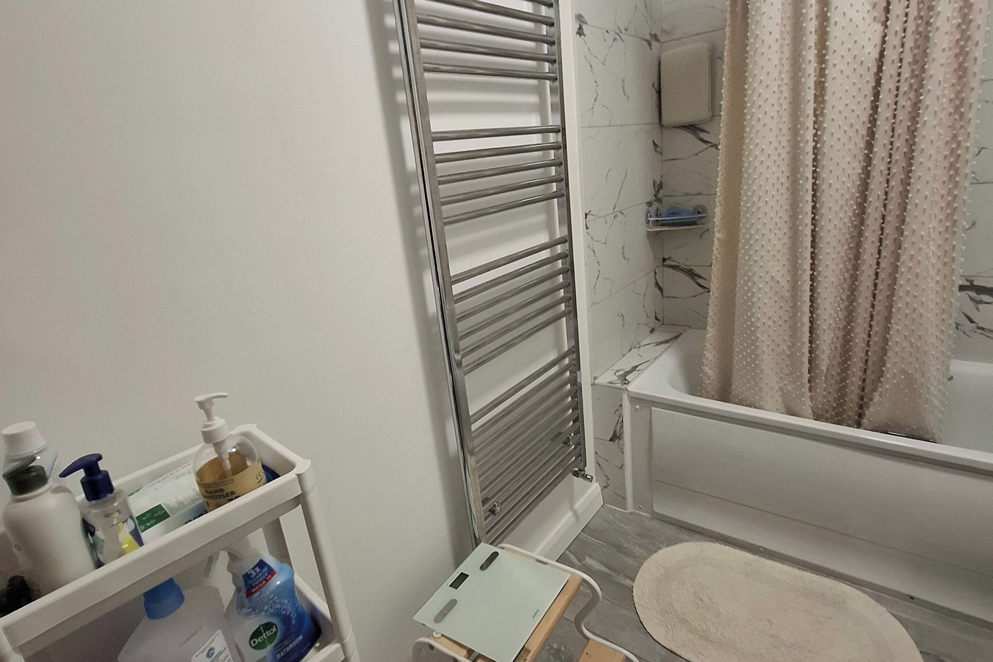 A bathroom with a white bathtub, a towel rack, a shower curtain, and a shelf with toiletries.