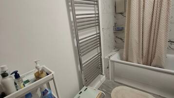 A bathroom with a white bathtub, a towel rack, a shower curtain, and a shelf with toiletries.