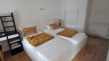 A bedroom with two beds, a wardrobe, a desk, and a chair.