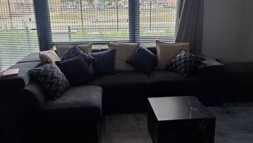 A sectional sofa with multiple cushions, a marble coffee table, and a view through a window with blinds.