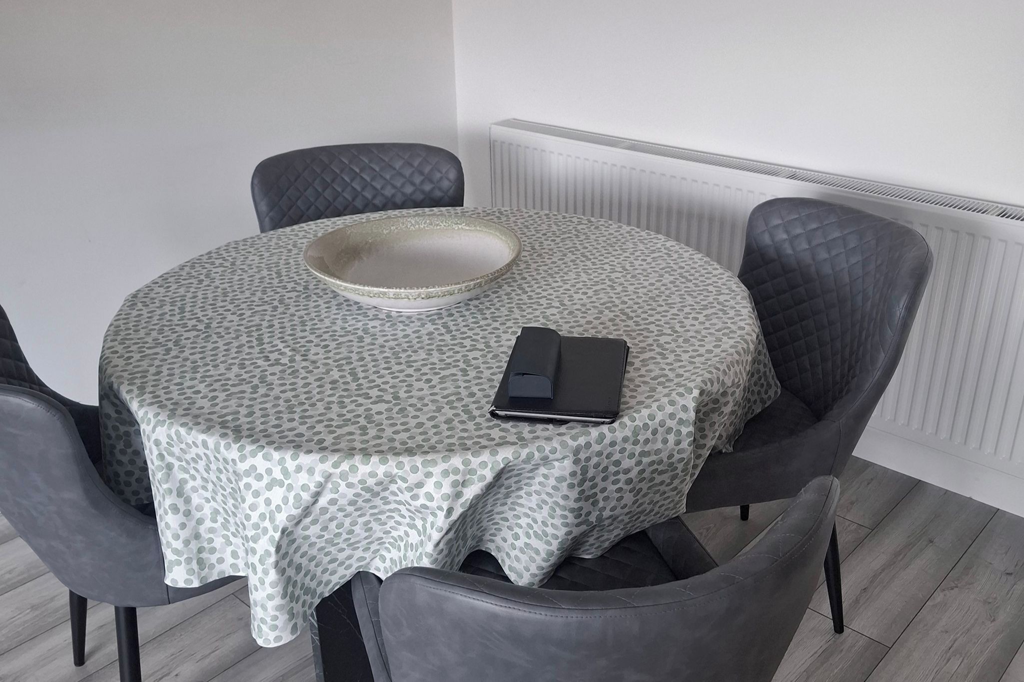A round dining table with a polka dot tablecloth, a white bowl, and a black wallet on it.