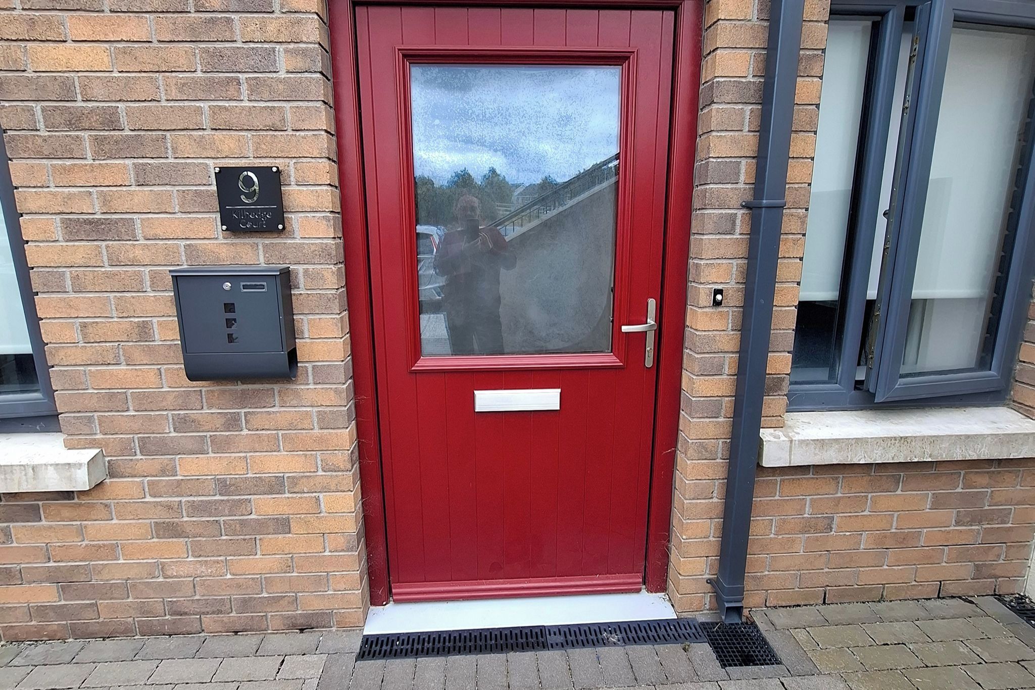 A red door with a glass panel, a mailbox, and a small plaque on a brick wall.
