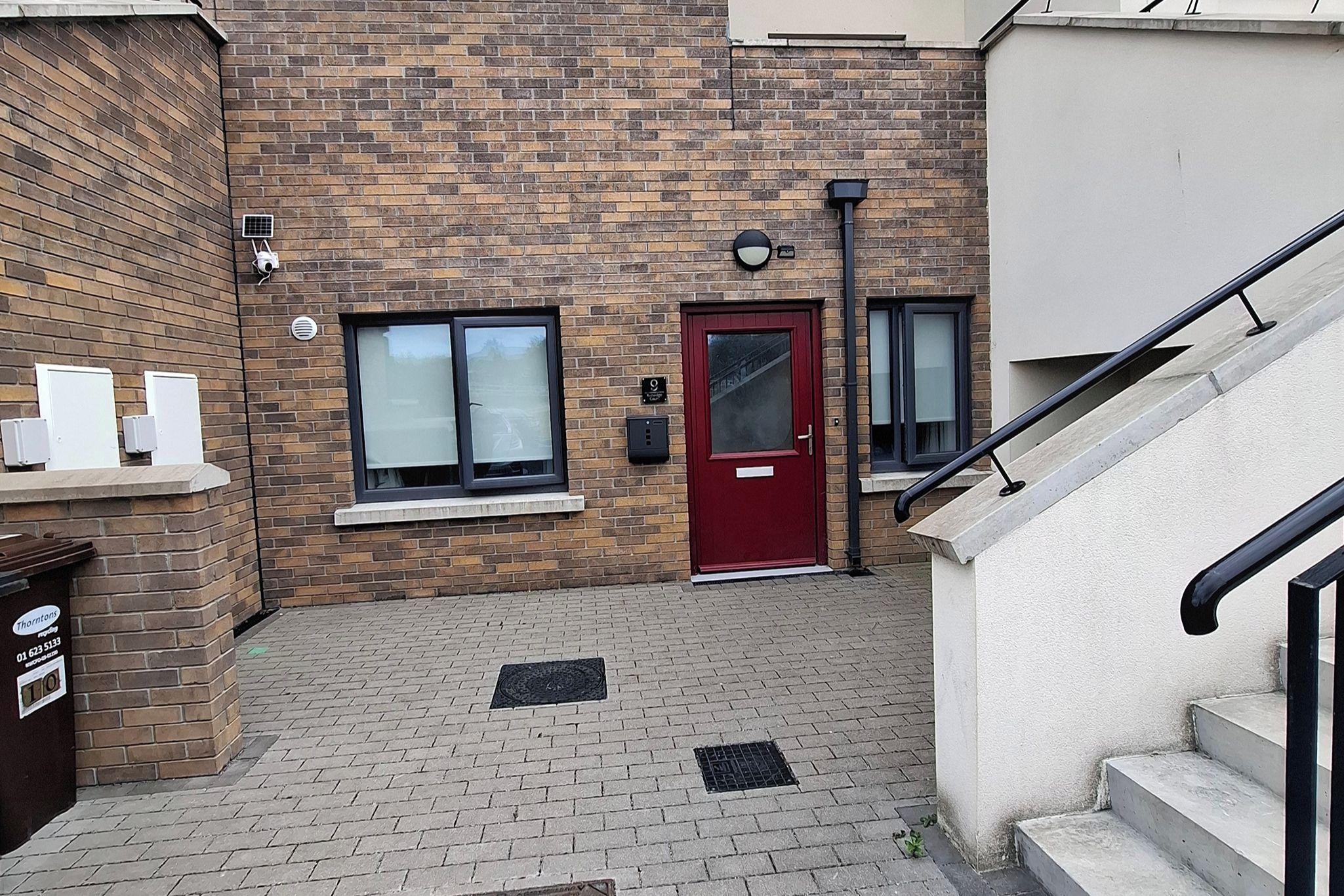 A brick building with a red door, windows, a mailbox, and a staircase.