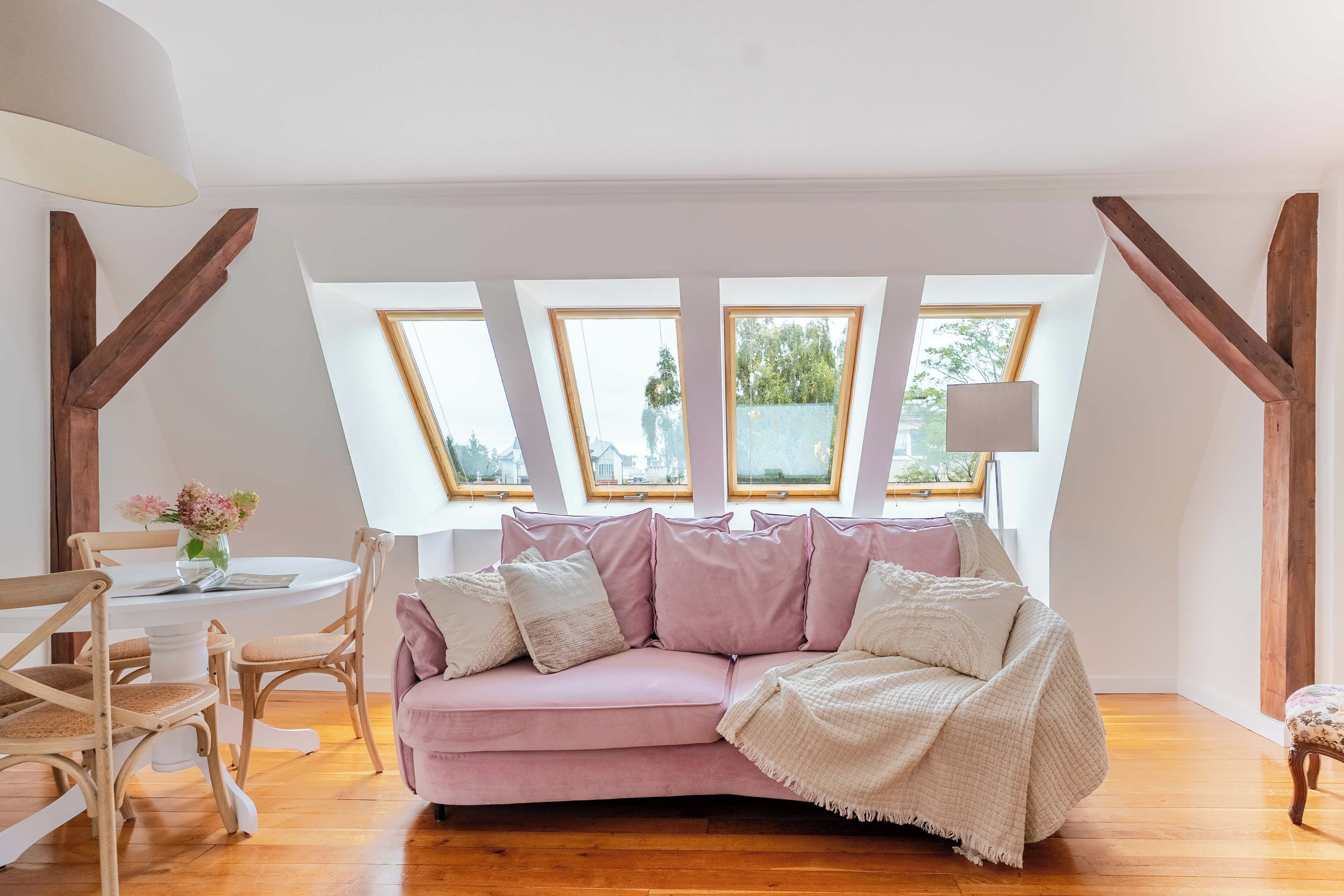 A cozy room with a pink sofa, wooden beams, and a view through skylights.