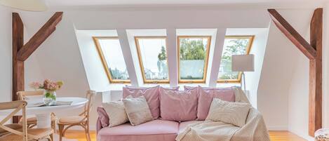 A cozy room with a pink sofa, wooden beams, and a view through skylights.