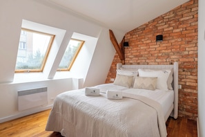 A bedroom with a sloped ceiling, a brick wall, a bed with white bedding, and two windows. - Seaside Loft Sopot - 5 min od plaży (Sopot)
