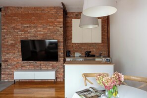 A modern living space with a brick wall, flat-screen TV, wooden flooring, and a dining area with a table and chairs. - Seaside Loft Sopot - 5 min od plaży (Sopot)