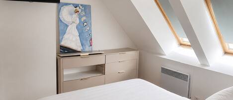 A bedroom with a bed, a dresser, a painting, and skylights.