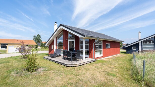 Une maison rouge avec un patio couvert et un ciel dégagé.
