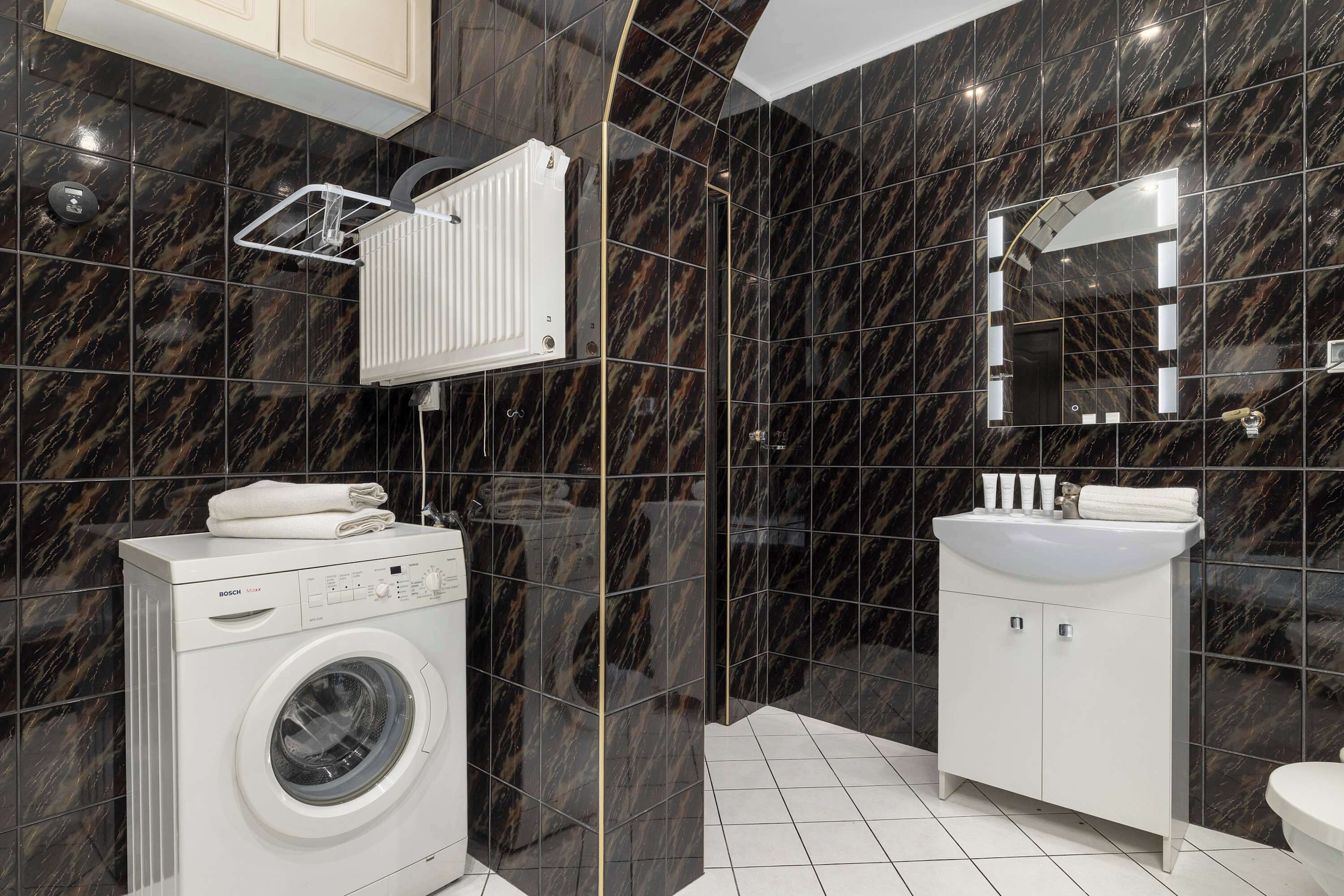 Une salle de bain moderne équipée d’un lave-linge intégré, d’un grand miroir et d’un lavabo blanc.