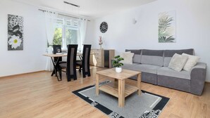 A modern living room with a grey sofa, wooden coffee table, and a dining area with a table and chairs.