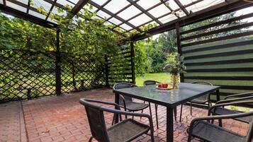 Eine Terrasse im Freien mit Tisch und Stühlen, umgeben von einer Holz-Pergola und einem Gitterzaun.