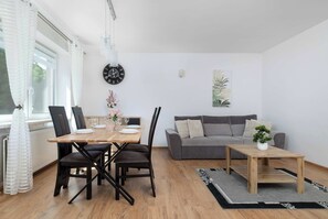 A modern living room with a dining area, grey sofa, wooden coffee table, and a clock on the wall. - Spacious House with Garden | Three Bedrooms | Garage (Wieliczka)