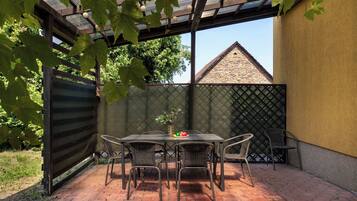 Une terrasse extérieure avec une table et des chaises, un espace abrité avec un toit en métal et un sol en briques.