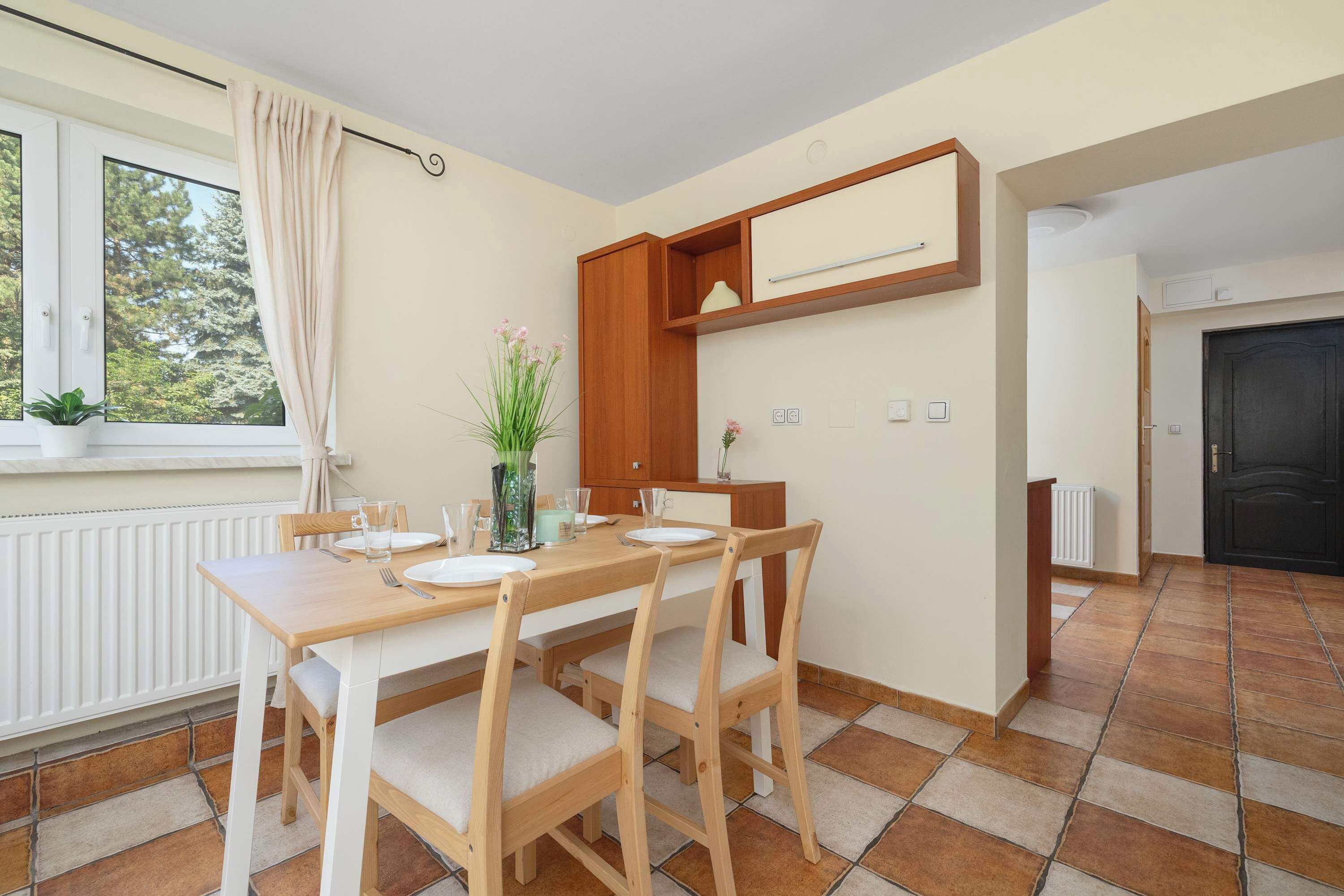 Un coin repas avec une table et des chaises en bois, une fenêtre avec des rideaux et un radiateur.