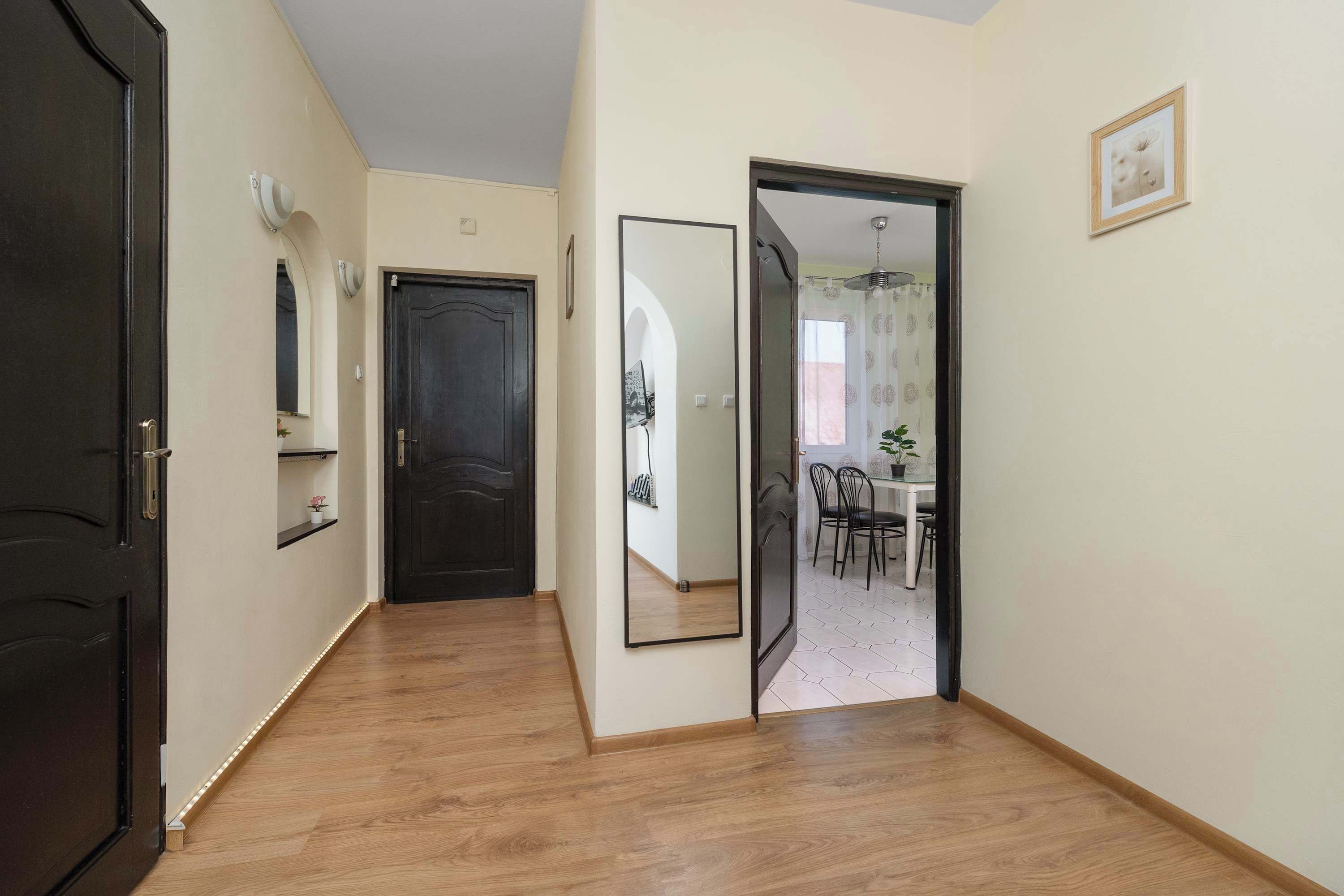 Un couloir avec un plancher en bois, une porte noire et un coin repas comprenant une table et des chaises.
