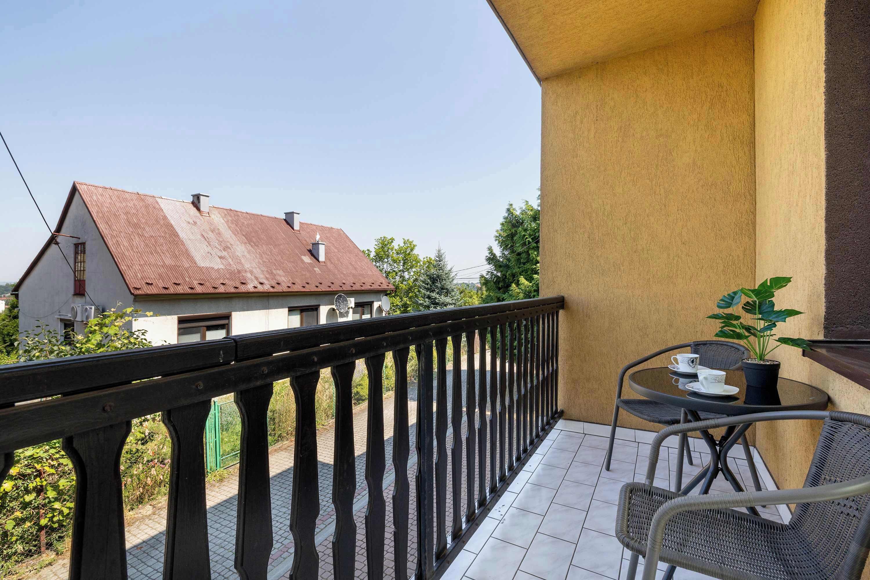 A balcony with a black railing, a small table with chairs, and a potted plant.