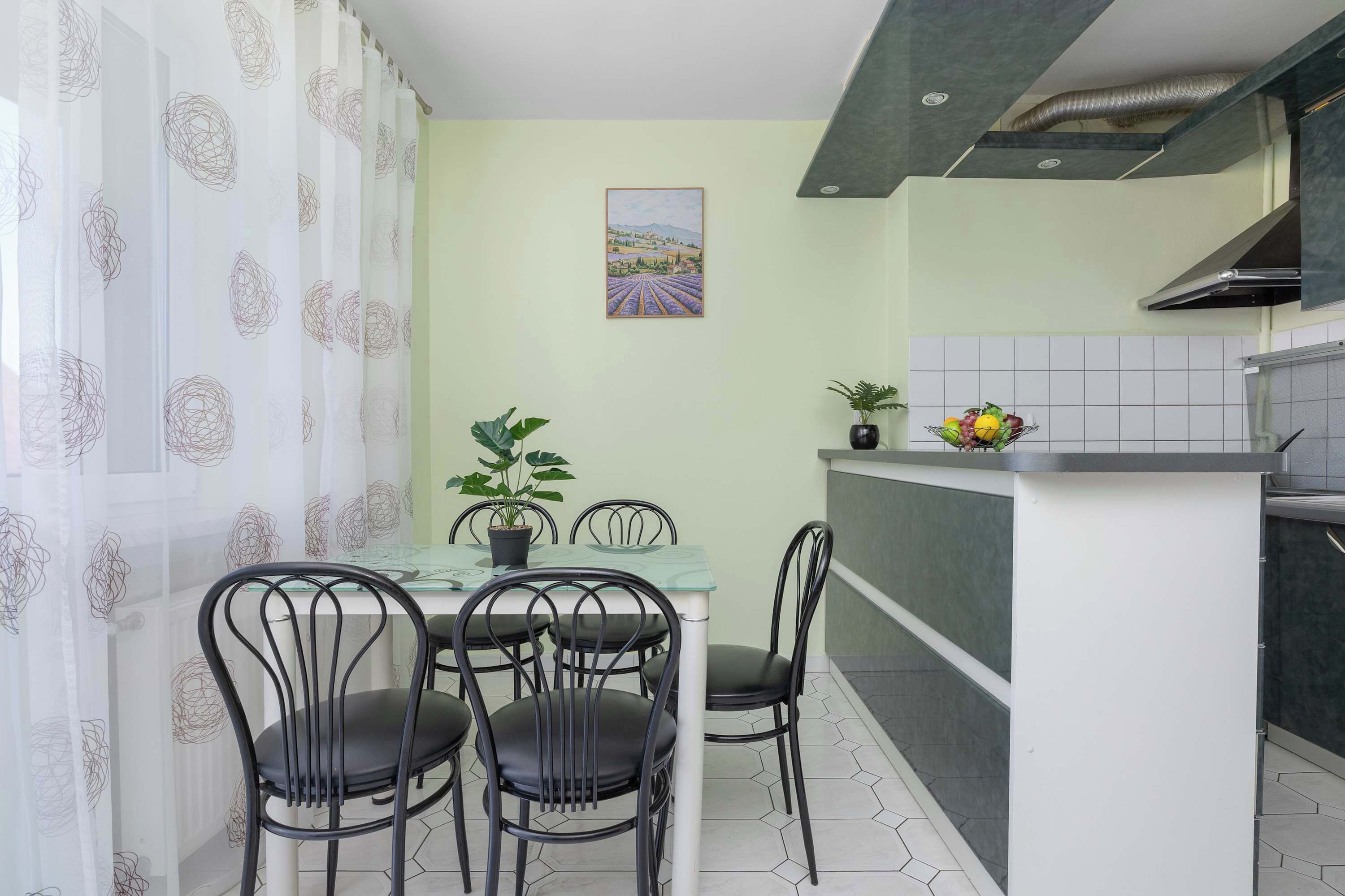 Eine kompakte Küche mit Essbereich, ausgestattet mit einem Tisch, Stühlen, einem Blumentopf und einer Obstschale auf der Arbeitsplatte.